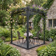 Shire 8x8 dark grey wooden pergola with integrated decking base and patio dining set in a lush garden