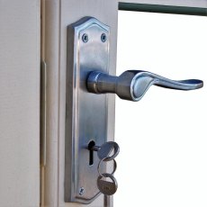 Close-up view of the metallic door handle mechanism with a key inserted in the lock on a light-colored frame.