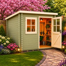 Exterior view of the sage green Shire Dean log cabin with its half-glazed door open to reveal interior shelving and garden storage, flanked by blooming flowers and pink tree blossoms.