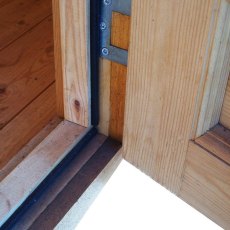 Close-up detail of the log cabin's open door threshold, showing the lower frame joint and weather seal.