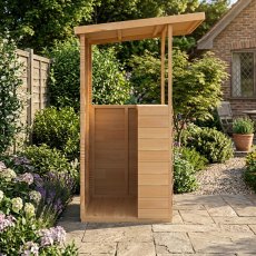 Side profile view of the wooden Shire Tiki Garden Bar standing on a stone patio surrounded by garden foliage.